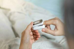 weiblich Hände mit ein Impuls Oximeter beim das Index Finger. Frau Lügen beim das Bett. Gadgets zum Gesundheit Pflege. Konzept von Entschlossenheit von Sauerstoff im das Blut. ShotlistGesundheit foto