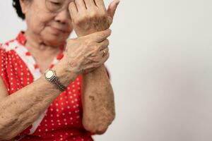 Alten asiatisch Frau Patienten leiden von Betäubung Schmerzen im Hände von rheumatoide Arthritis. Senior Frau Massage ihr Hand mit Handgelenk Schmerz. Konzept von Joint Schmerz, rheumatoide Arthritis, und Hand Probleme. foto