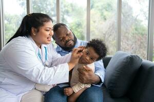 pädiatrisch Arzt Prüfung Ohr zum ein Hören Prüfung Prüfung süß wenig Mädchen im medizinisch Gesundheitswesen Krankenhaus oder Klinik. lächelnd afrikanisch amerikanisch Baby weiß Kinderarzt im Krankenhaus foto