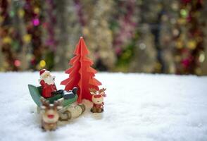 sata Sitzung auf Weiß Schnee mit Gruppe von Geschenke im Vorderseite von rot Origami Weihnachten Baum warten zum komisch Festival, Weihnachten und Neu Jahr Konzept. foto