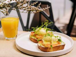 Brot Toast mit zerschlagen Avocado, Lachs und pochiert Ei und Orange Saft foto