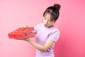 Porträt eines fröhlichen Mädchens, das in der Hand eine Geschenkbox öffnet, isoliert auf rosa Hintergrund foto