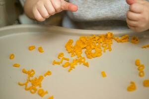 Hand von Kind Sammeln Briefe von Pasta von Tisch. Entwicklung von fein Motor- Kompetenzen von Hände. montessori Technik. lernen Briefe und Alphabet im Spiel foto