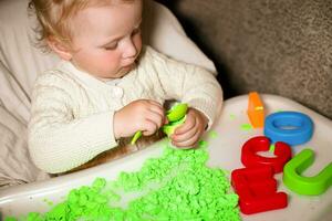 Mädchen Theaterstücke mit kinetisch Sand. Kind baut Hirten im bilden von Briefe von Sand. früh Entwicklung von Kinder. fein Motor- Kompetenzen von das Finger. foto