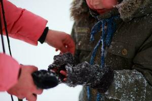 Mama setzt Handschuhe auf ihr Söhne Hände im Park im Winter. ein Kind im warm Kleider im das Winter nach ein Schneefall. das Junge ist kalt im eisig Wetter. foto