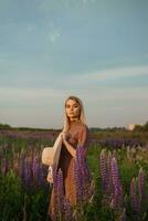 ein schön Frau im ein Stroh Hut Spaziergänge im ein Feld mit lila Blumen. ein gehen im Natur im das Lupine Feld foto