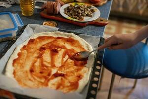 Herstellung hausgemacht Pizza von Hefe Teig. Kind Abstriche Pizza mit Tomate Soße beim Zuhause auf Tisch. Lebensstil Konzept. hausgemacht Essen auf Selbstisolation während Coronavirus foto