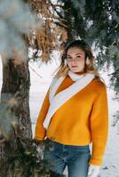 Teen blond im ein Gelb Sweatshirt draußen im Winter. ein Teenager Mädchen auf ein gehen im Winter Kleider im ein schneebedeckt Wald foto