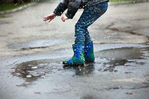 Junge im Blau mit Grün Gummi Stiefel gesprungen in tief Pfütze. foto