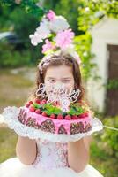 Mädchen halten Geburtstag Kuchen mit Nummer 8 und Inschrift glücklich Geburtstag. feiern zeremoniell Veranstaltungen auf Straße während Quarantäne. Kind im Hintergrund dekoriert Foto Zone von Blumen.