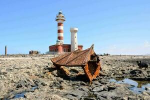 ein alt Boot ist Sitzung auf das Felsen in der Nähe von ein Leuchtturm foto