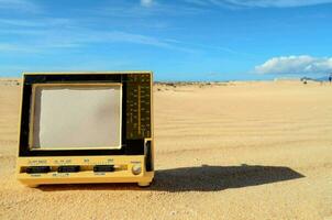 ein klein Gelb Fernsehen Sitzung im das Sand foto