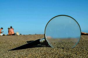 ein Vergrößerung Glas auf das Strand mit Menschen im das Hintergrund foto