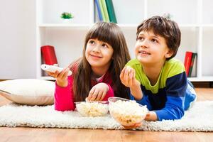 zwei Kinder sind Verlegung auf das Fußboden mit Popcorn und Aufpassen Fernseher foto