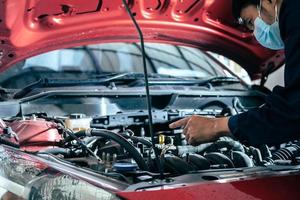 asiaten mann medizinische schützen schutzmaske gesichtsmaske mechanikerinspektion halten schlüssel für fix blaues auto für service wartungsversicherung mit auto motorhaube auto foto