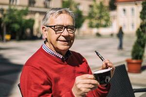 heiter Senior Mann genießt Trinken Kaffee und Rauchen elektronisch Zigarette beim das Bar foto