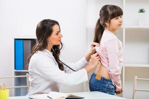 weiblich Arzt Hören Lunge von ein wenig Mädchen mit Stethoskop beim medizinisch Büro foto