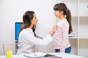 weiblich Arzt Hören Herzschlag von ein Kind mit Stethoskop beim medizinisch Büro foto