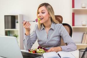 schön Geschäftsfrau genießt Essen Salat während Arbeiten im ihr Büro foto
