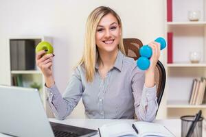 schön Geschäftsfrau halten Apfel und Gewichte während Arbeiten im ihr Büro foto