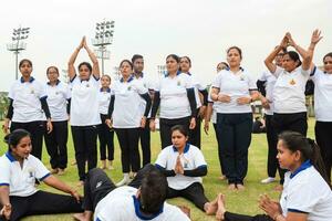 Neu Delhi, Indien, Juni 21, 2023 - - Gruppe Yoga Übung Session zum Menschen beim Yamuna Sport Komplex im Delhi auf International Yoga Tag, groß Gruppe von Erwachsene Teilnahme Yoga Klasse im Kricket Stadion foto