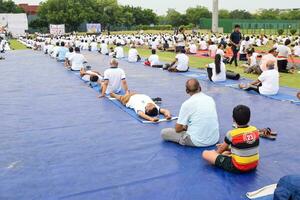 Neu Delhi, Indien, Juni 21, 2023 - - Gruppe Yoga Übung Session zum Menschen beim Yamuna Sport Komplex im Delhi auf International Yoga Tag, groß Gruppe von Erwachsene Teilnahme Yoga Klasse im Kricket Stadion foto