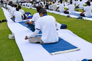 Neu Delhi, Indien, Juni 21, 2023 - - Gruppe Yoga Übung Session zum Menschen beim Yamuna Sport Komplex im Delhi auf International Yoga Tag, groß Gruppe von Erwachsene Teilnahme Yoga Klasse im Kricket Stadion foto