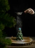 Hand Sträusel Glasur Zucker auf Lebkuchen Baum auf dunkel Hintergrund. Urlaub und Weihnachten Konzept. hoch Qualität Foto