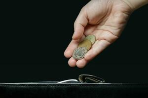 ein unsichtbar Frau Hand setzt ein Münzen im ein wallet.a schwarz Hintergrund foto