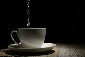 Tasse und Untertasse in welche Wasser ist gegossen auf hölzern Tabelle beim Dämmerung. selektiv Fokus foto