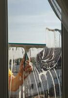 ein Mann wäscht ein Fenster auf ein Balkon auf ein sonnig Tag. foto