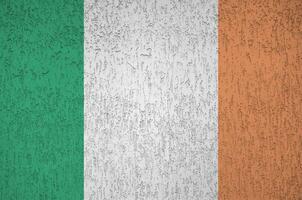 irland-flagge in hellen farben auf alter reliefputzwand dargestellt. strukturierte Fahne auf rauem Hintergrund foto