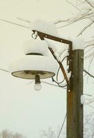 eine Holzsäule mit einer Hängelampe. der plafond der lampe ist mit einer dicken schneeschicht bedeckt foto