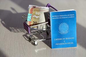 Brasilianer Arbeit Karte und Sozial Sicherheit Blau Buch und reais Geld Rechnungen im Einkaufen Wagen foto