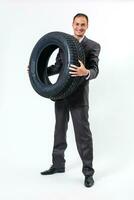 voll Länge Porträt von ein jung Geschäftsmann gelehnt auf ein Stapel von Auto Reifen isoliert auf Weiß Hintergrund foto