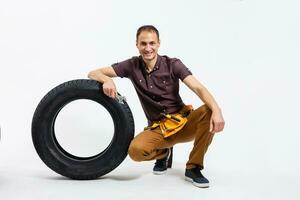 ein männlich Mechaniker posieren mit ein schonen Reifen und halten ein Schlüssel isoliert auf Weiß Hintergrund foto