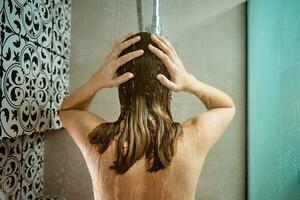 zurück Aussicht von Frau nehmen ein Dusche im Badezimmer foto