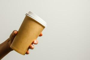 Frau halten im Hand Papier Tasse mit Kaffee oder Tee. trinken Kaffee Zeit. Einweg Papier Tasse. schön blond Haar jung Mädchen. beiläufig Stil, Weiß Hemd und Jeans. nehmen weg. heiß Getränk. leer Raum foto