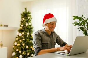 Mann im Santa claus Hut halten Laptop mit fröhlich Weihnachten Tippen foto