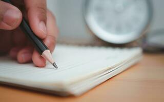Mensch Hände Schreiben Anmerkungen mit Bleistift auf Papier auf hölzern Tabelle Oberfläche. foto