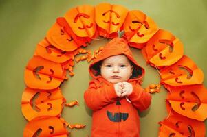 Halloween Porträt von bezaubernd Baby Lügen auf Grün Hintergrund Nächster zu Kürbis Girlande foto