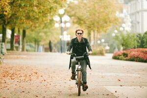 draussen Porträt von gut aussehend lesehaarig Mann Reiten Fahrrad im ein Stadt foto