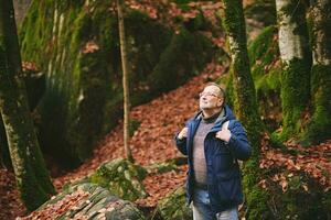 gut aussehend Mitte Alter Mann Wandern im Wald, tragen warm Jacke, Rucksack und Brille foto