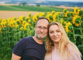 draussen Porträt von Mitte Alter Paar genießen nett Tag im Landschaft, posieren Nächster zu Sonnenblume Feld foto