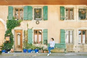 jung schwanger Frau Sitzung auf Bank Nächster zu schön Dorf Haus Fassade foto