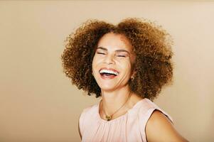 Mode Studio Porträt von stilvoll Mitte Alter Frau posieren auf Beige Hintergrund, Lachen 50 - - 55 Jahr alt Dame mit lockig Haar foto