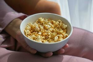 jung Frauen Essen Popcorn Sitzung auf Sofa beim Zuhause foto