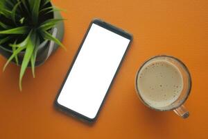 Clever Telefon mit leeren Weiß Bildschirm und Tasse von Kaffee auf Tabelle foto