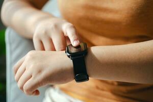 jung Frau suchen und mit ein Smartwatch, weiblich Sitzung auf das Sofa Überprüfung ihr Smartwatch. foto