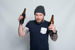 brutal bärtig männlich mit tätowiert Arm Getränke ein Bier von ein Flasche. foto